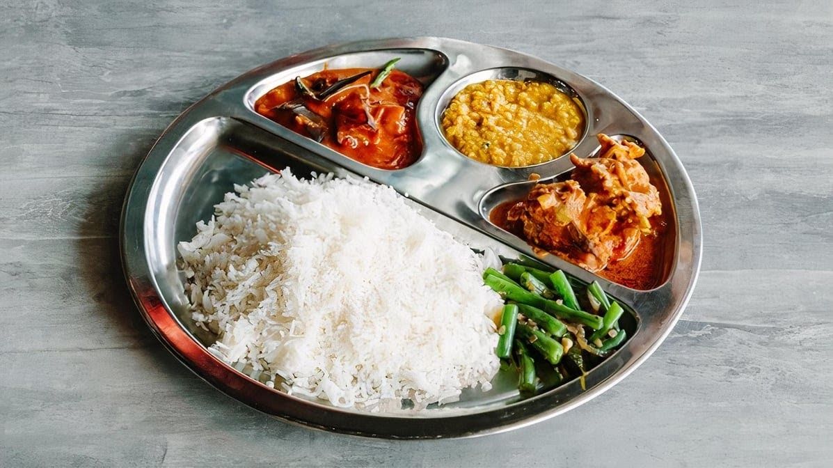 South Indian steel thali plate with rice, two curries, dhal and stir-fried green beans on grey stone