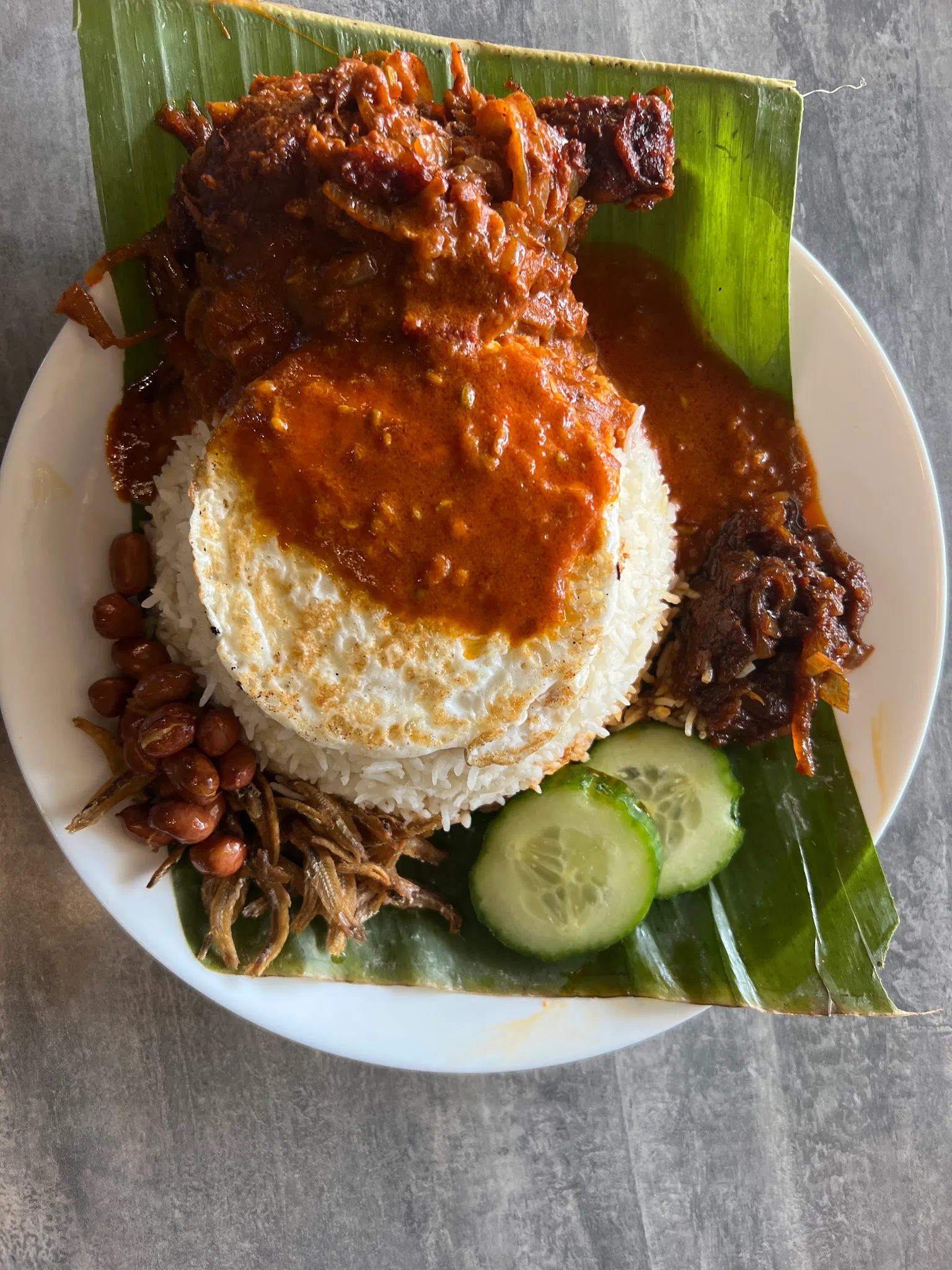Nasi lemak on banana leaf with beef rendang, sambal, dried anchovies, peanuts and sliced cucumber