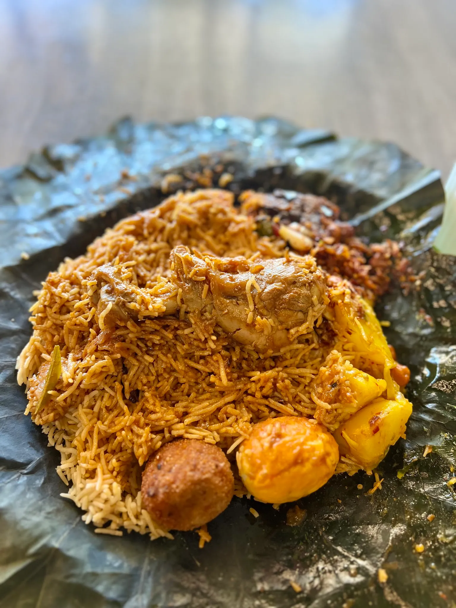 Chicken biryani on banana leaf with fragrant spiced rice, bone-in chicken, fried egg and potato
