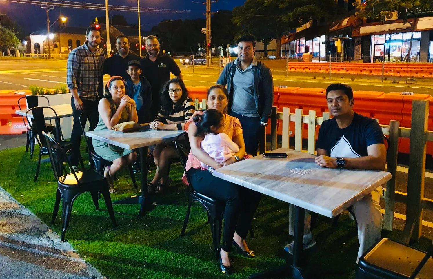 Group of customers seated at outdoor tables along a lit street at night