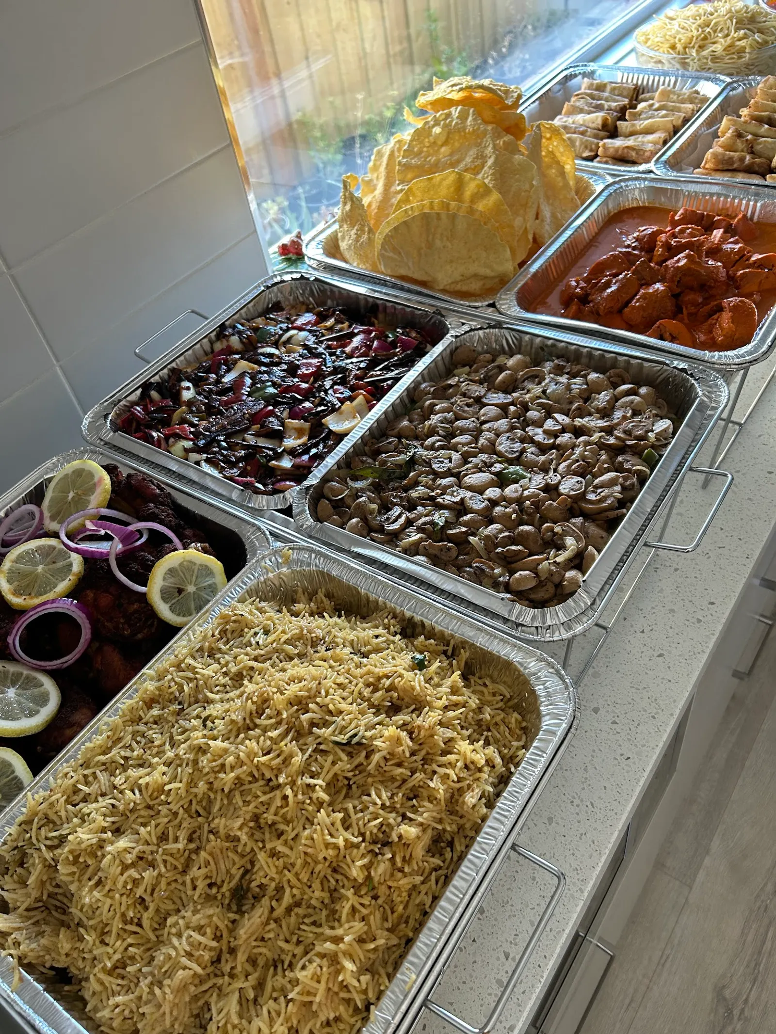 Catering spread in foil trays — biryani, mixed bean salad, papadums and lacework bread