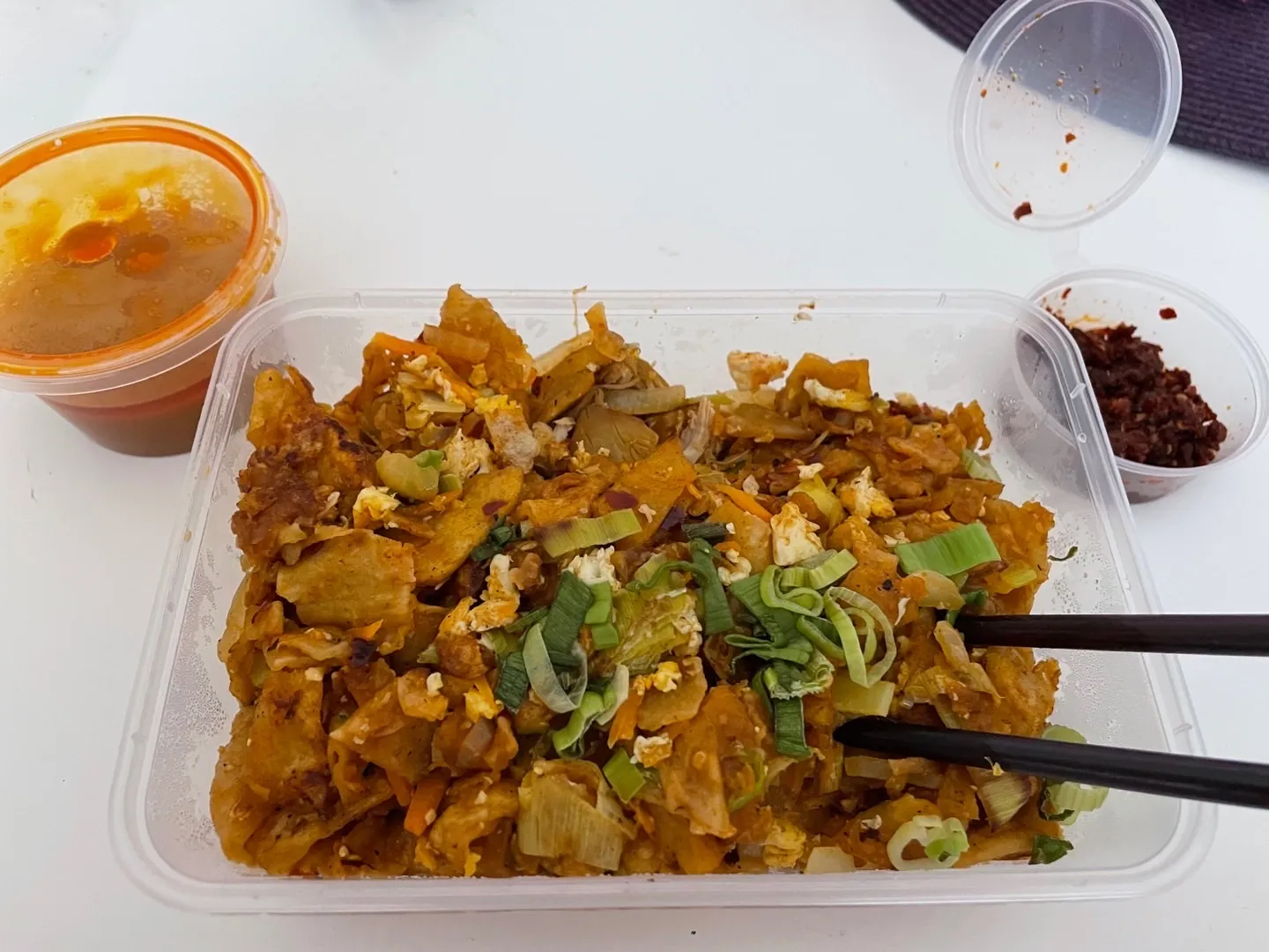 Kothu roti in clear takeaway container with dipping sauce and chilli flakes