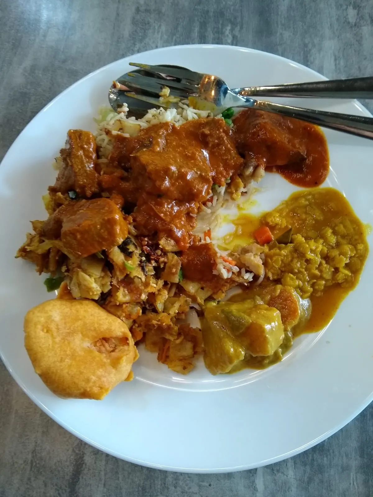 Mixed rice plate with curry, kothu, okra, dhal and fried puri on white plate