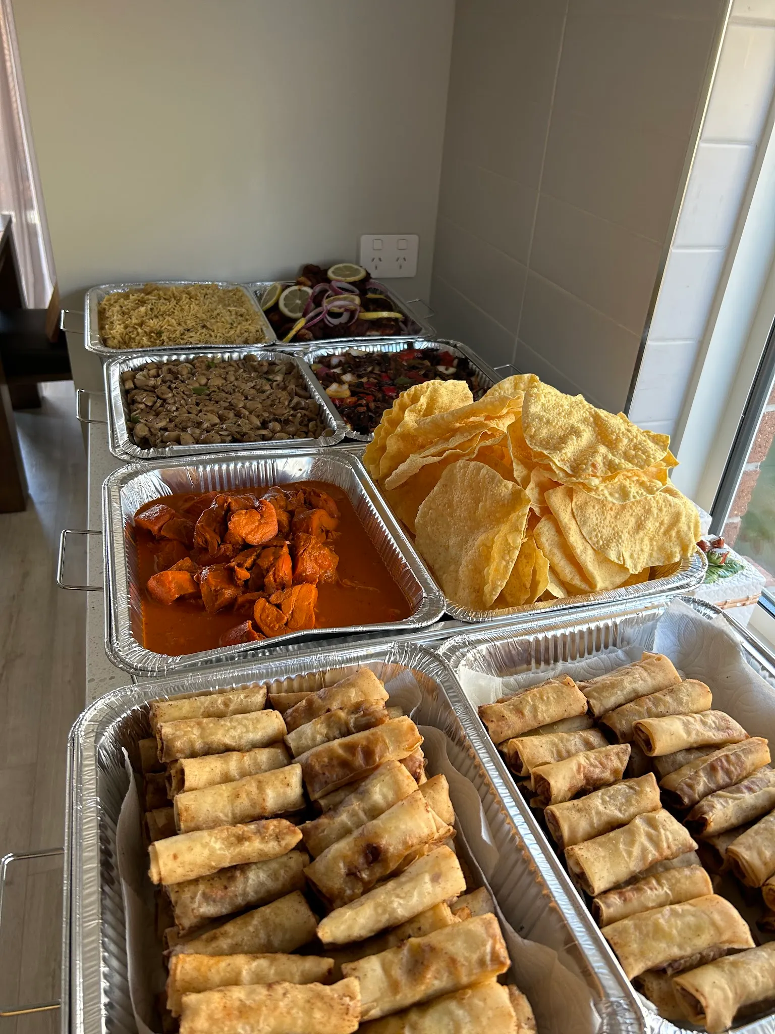 Indoor catering spread in foil trays with spring rolls, red chicken curry, papadums and biryani
