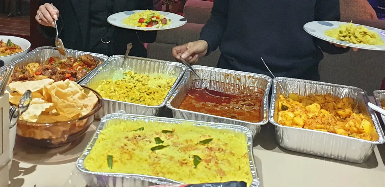 Guests serving themselves at a catering event from trays of biryani, curry and papadums