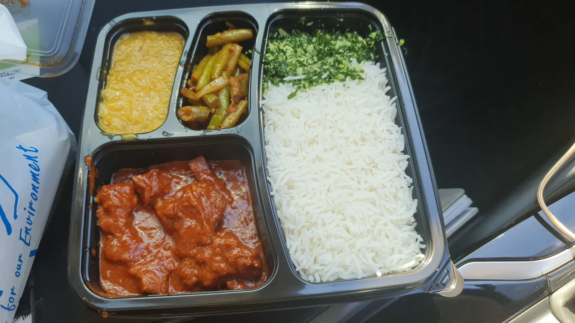 Takeaway meal tray with rice, butter chicken, dhal and vegetables on a car seat