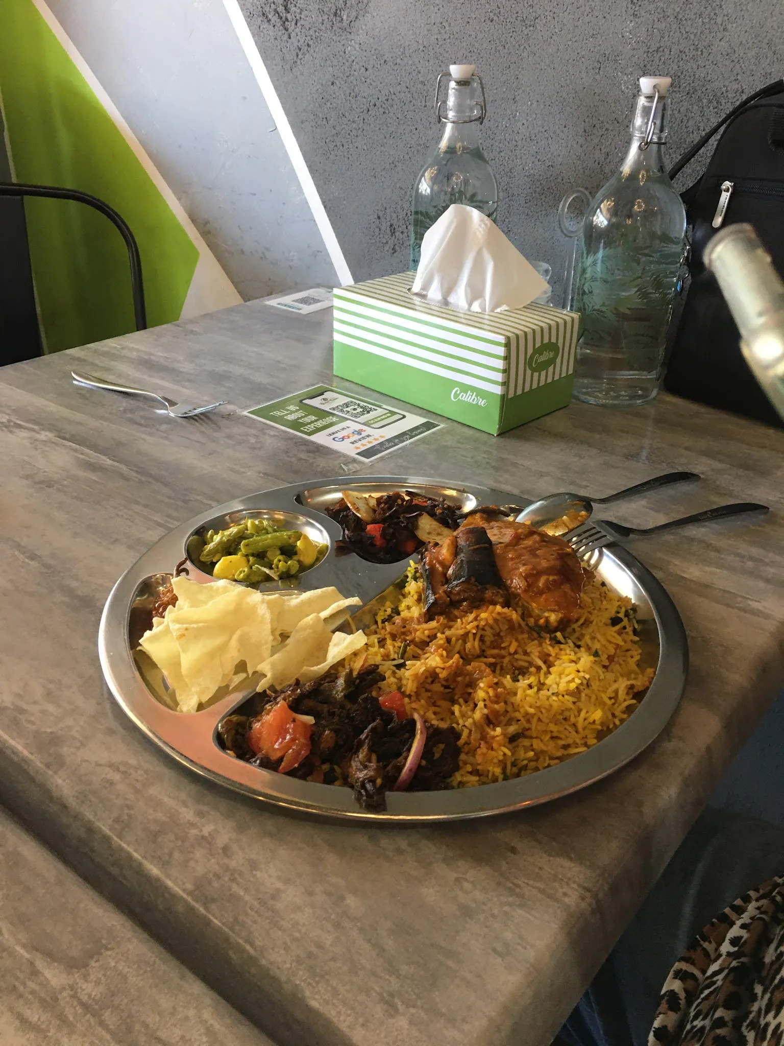 Stainless steel thali with biryani, chicken and curry on outdoor concrete table