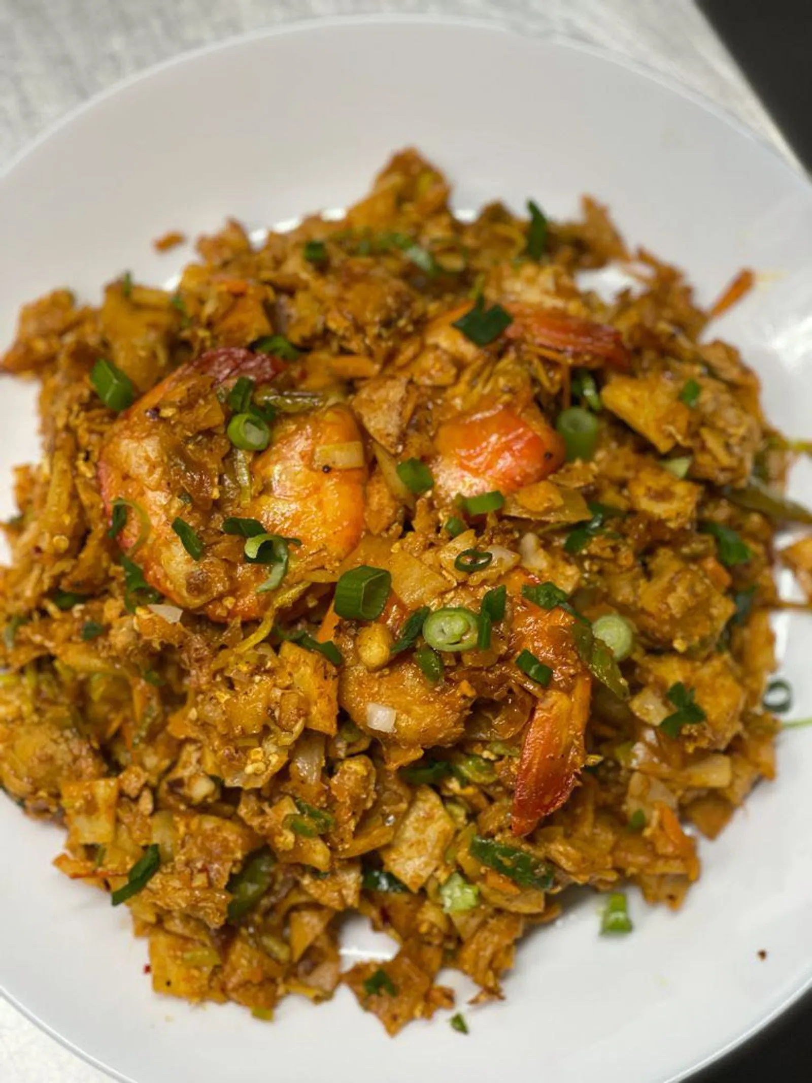 Prawn kothu roti in white bowl with king prawns and spring onion garnish