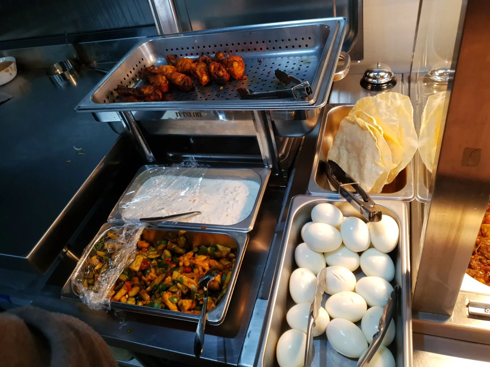 Food truck bain-marie station with fried chicken, stir-fried vegetables, eggs and papadums under warm hood lighting